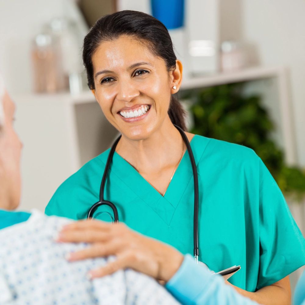 A smiling caregiver in teal scrubs comforting a resident